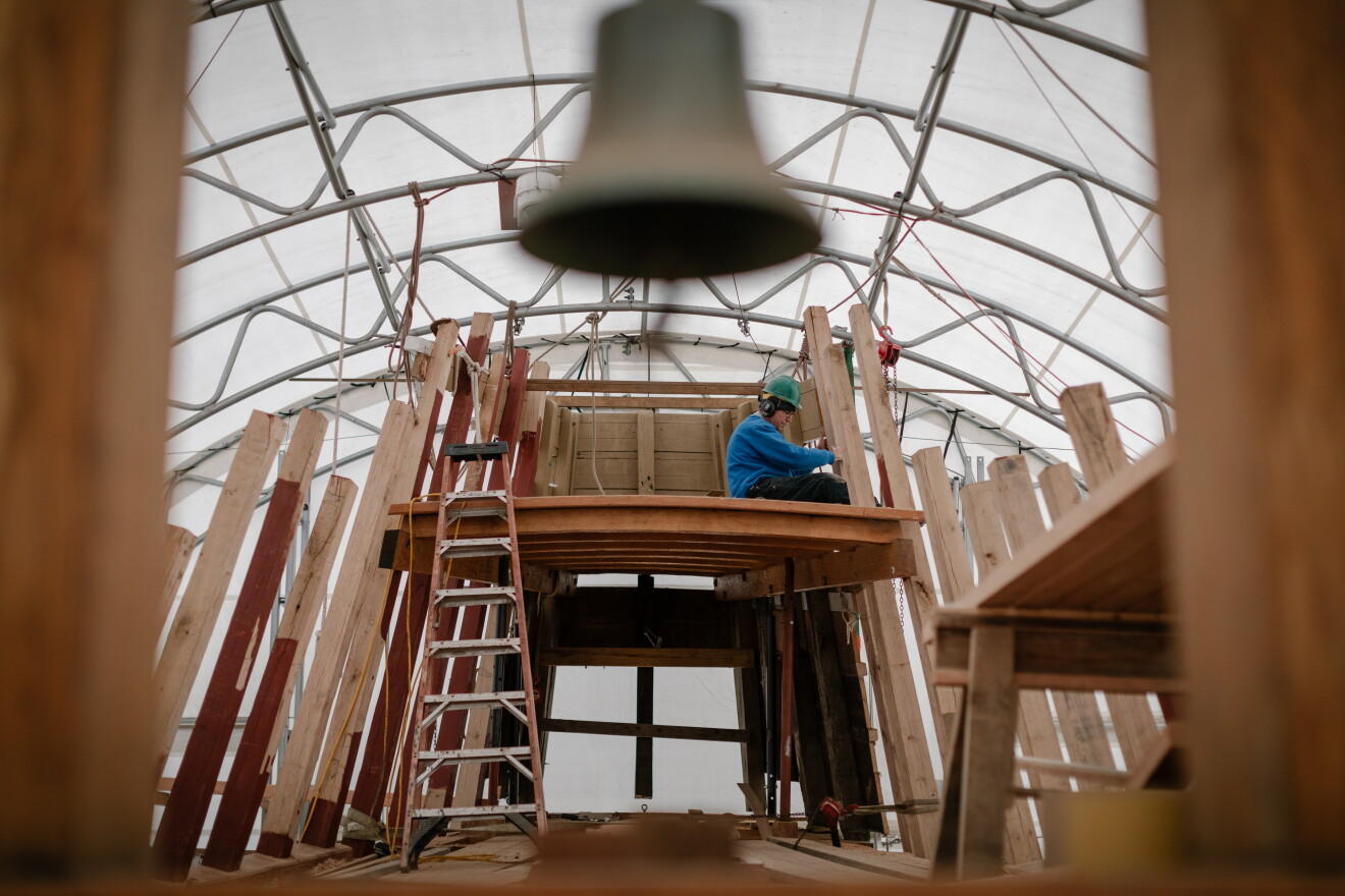 A Mystic Seaport Museum shipwright works on Mayflower's restoration, seen through the ship's belfry.